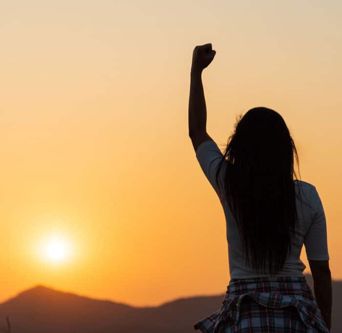 Soft focus of woman with fist in the air during sunset sunrise mountain in background.