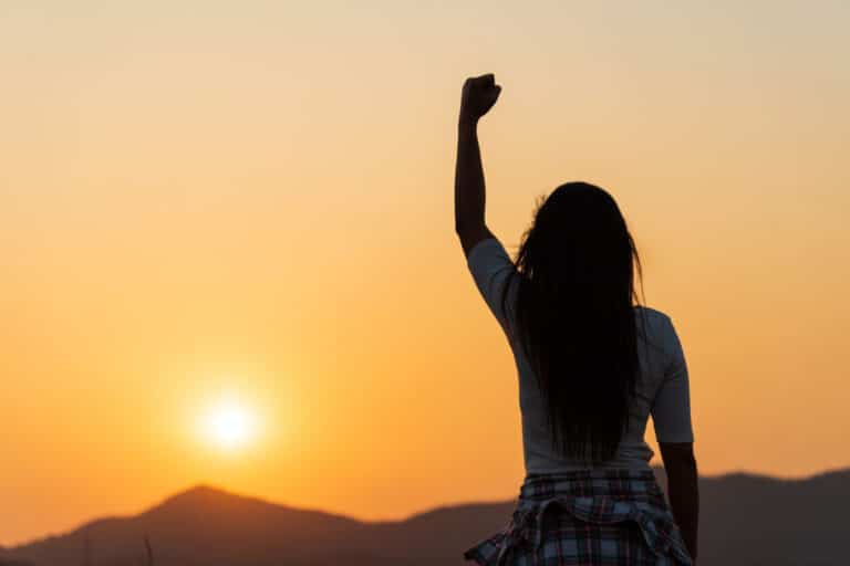 Soft focus of woman with fist in the air during sunset sunrise mountain in background.