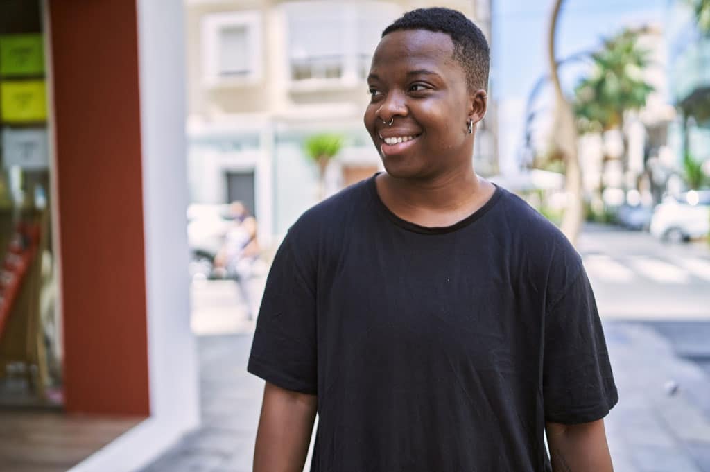 Young African American transgender individual smiling confidently while walking down the street.
