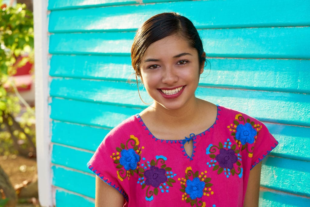 Mexican latin woman wearing mayan dress smiling in front of turquoise wall